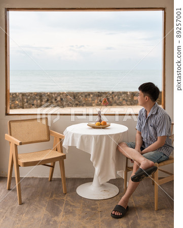 Young asian man sitting and looking at the beach from the window on weekend 89257001