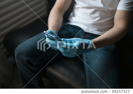 A man uses a smartphone while sitting on the couch. Blue latex gloves and white jersey A man uses a smartphone while sitting on the couch. Blue latex gloves and white jersey 89257327