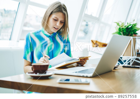 Student reading book and using laptop in cafe Student reading book and using laptop in cafe 89257558