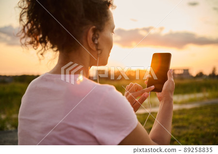 Focus on athlete hands putting finger on smartphone with blank black screen with copy ad space formobile fitness app on sunset and nature background Focus on athlete hands putting finger on smartphone with blank black screen with copy ad space formobile fitness app on sunset and nature background 89258835