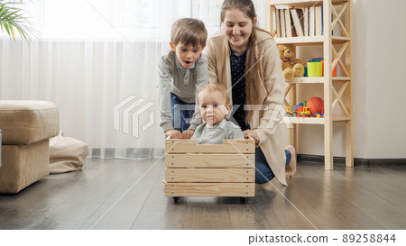 Cute baby boy sitting in wooden toy box while his family riding him at living room. 89258844