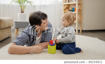 Cute baby boy playing with toys and his father on carpet at home. 89258911