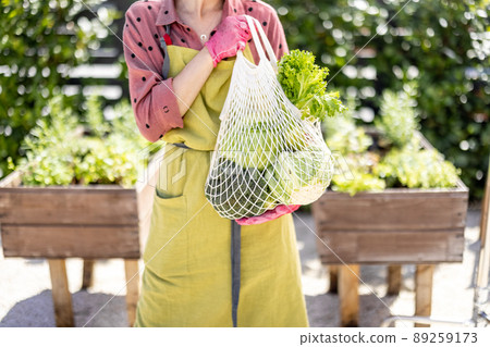 Holding mesh bag full of fresh vegetables and greens at home garden Holding mesh bag full of fresh vegetables and greens at home garden 89259173