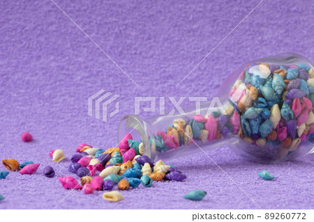 A transparent vessel lies on a lilac background. There are colorful shells in a jar. The concept of memories of summer holidays and the sea 89260772