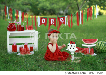 A festive picnic for the first birthday with decor, garland, lemonades and watermelons. The girl tries her birthday cake. A holiday in nature in the garden A festive picnic for the first birthday with decor, garland, lemonades and watermelons. The girl tries her birthday cake. A holiday in nature in the garden 89261504