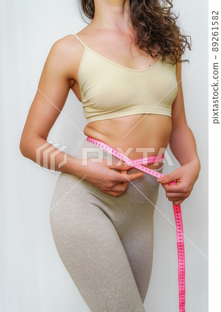Close up of slim woman measuring her waist's size with tape measure. Isolated on white background. Close up of slim woman measuring her waist's size with tape measure. Isolated on white background. 89261582