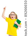 Idea. Points a finger up. Cheerful young child girl with glasses holding a book to study isolated on a white background. 89266650