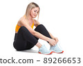 A beautiful, athletic, slim, smiling and cheerful woman in an orange top and black sweatpants is sitting and tying her shoelaces on sports sneakers. Lifestyle concept with sports and gym, healthy 89266653