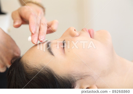 靠近額頭的手和一位年輕女子與美學家一起塗抹乳霜 89268860