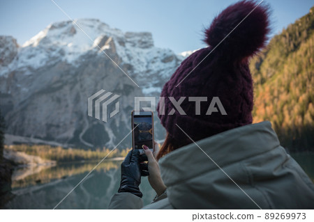 Dolomites nature. Lago di braies lake. Huge beautiful mountains. A woman in a purple hat taking a photo on the view Dolomites nature. Lago di braies lake. Huge beautiful mountains. A woman in a purple hat taking a photo on the view 89269973