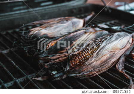 slightly charred sweet corn on the cob with husk on resting on a grill grate slightly charred sweet corn on the cob with husk on resting on a grill grate 89271525