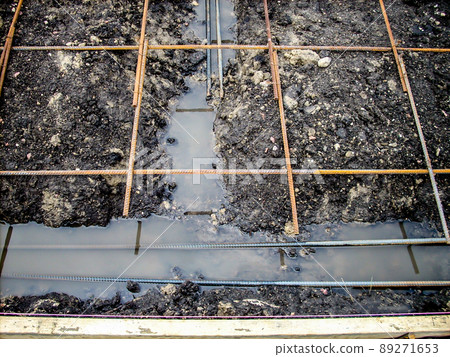 Construction site rebar suspended over a footing trench filled with rain water. Construction site rebar suspended over a footing trench filled with rain water. 89271653
