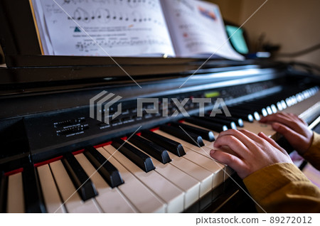 Young child practicing playing a piano with hands resting on keys 89272012