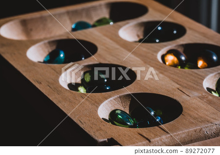Selective focus on glass beads on a wooden mancala board Selective focus on glass beads on a wooden mancala board 89272077