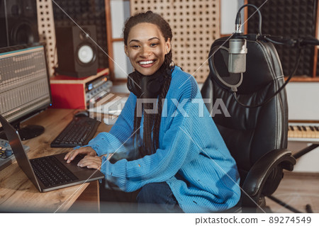 Charming sound engineer with beautiful toothy smile looking at camera while working on laptop in music recording studio 89274549