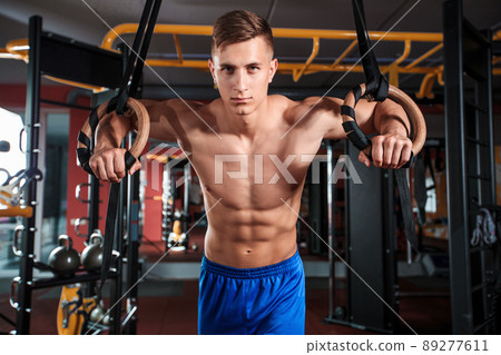Portrait of young man using gymnastic rings while exercising in gym 89277611