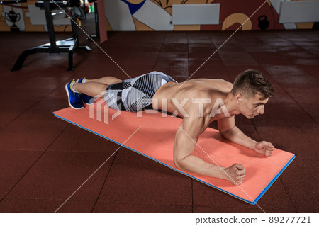 Confident muscled young man wearing sport wear and doing plank position while exercising on the floor at the gym 89277721