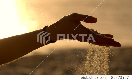 Young woman playing with sand on a beach at sunset - slow motion Young woman playing with sand on a beach at sunset - slow motion 89278507