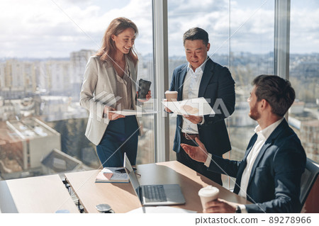 Positive office employees discussing work issues using laptop and documents with graphs  89278966