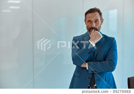 Thoughtful businessman scrutinising the camera against a white wall 89278988