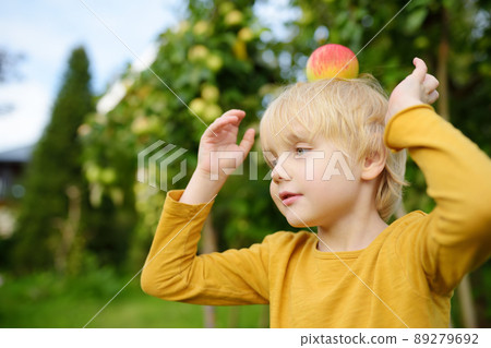 Little boy having fun with apple on head in domestic garden. Kids game at summer outdoors. 89279692