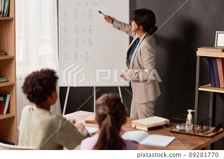 Hispanic teacher with hairbun pointing at whiteboard while working with kids in classroom 89281770