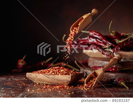 Chilli flakes are poured into a wooden dish. 89283287