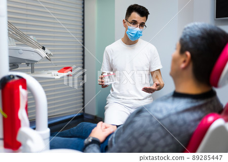 Dental surgeon with dental crown in hands model talks to patient about prosthetics. Man at the dentist's appointment 89285447