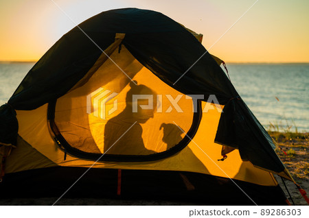 Woman and dog in a tourist tent at sunset. Camping with a pet 89286303