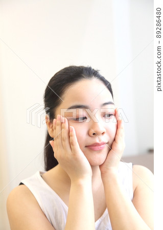 Young woman looking down to touch her cheeks 89286480