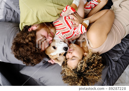 High angle view of multiethnic couple embracing their dog in costume with both sides and sleeping High angle view of multiethnic couple embracing their dog in costume with both sides and sleeping 89287228