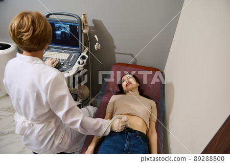 Brunette woman is examined by doctor, undergoes ultrasound examination of abdominal cavity and small pelvic organs on modern ultrasound machine Brunette woman is examined by doctor, undergoes ultrasound examination of abdominal cavity and small pelvic organs on modern ultrasound machine 89288800