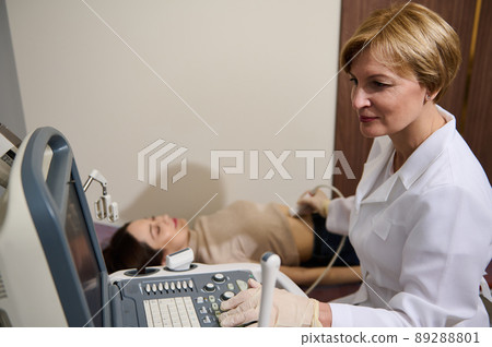 Confident European mature doctor doing ultrasound examination in early pregnancy to young woman in gynecological clinic Confident European mature doctor doing ultrasound examination in early pregnancy to young woman in gynecological clinic 89288801
