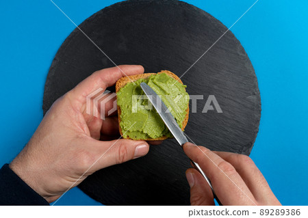 Avocado toast. Man's hands spreading avocado paste on a slice of bread. Healthy food concept, top view 89289386