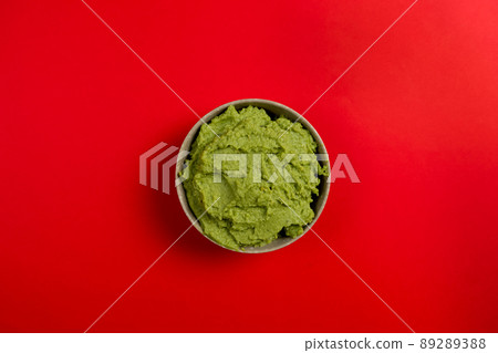 Top view of a ceramic bowl filled with the succulent guacamole sauce of Mexican origin on a red background. 89289388