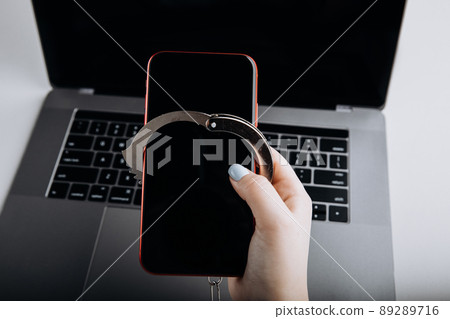 Concept of smartphone addiction. Phone chained to handcuff in hand with laptop background 89289716