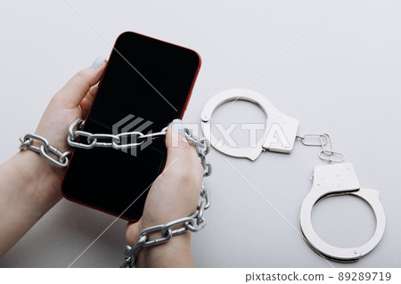Smartphone with chain locked and handcuffs in woman's hand. Information security or smartphone addiction concept 89289719
