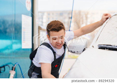 self-service car wash. a man in a work jumpsuit washes the car with a sponge self-service car wash. a man in a work jumpsuit washes the car with a sponge 89294320
