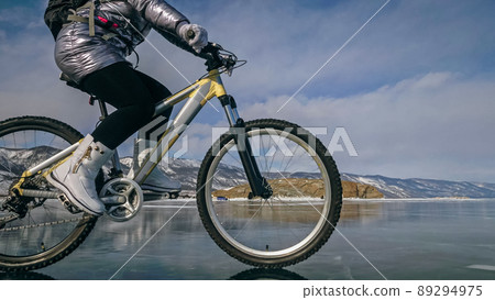 Woman is riding bicycle on the ice. Tires on bike are covered wi Woman is riding bicycle on the ice. Tires on bike are covered wi 89294975