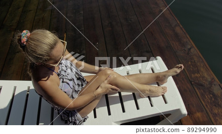 Woman lie on a sunbed in sunglasses and a boho silk shawl. Girl rest on a flood wood underwater pier. The pavement is covered with water in the lake. Woman lie on a sunbed in sunglasses and a boho silk shawl. Girl rest on a flood wood underwater pier. The pavement is covered with water in the lake. 89294990