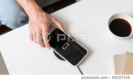 Technology Concept A person with his light blue jeans sitting on the couch and trying to charge his smartphone on the wireless battery charger Technology Concept A person with his light blue jeans sitting on the couch and trying to charge his smartphone on the wireless battery charger 89297348