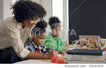 African American female teacher standing with pupils teaching writing lesson in modern classroom. African American female teacher standing with pupils teaching writing lesson in modern classroom. 89297819