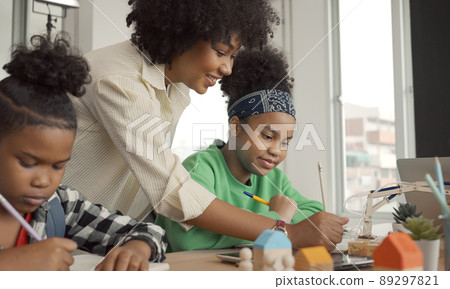 African American female teacher standing with pupils teaching writing lesson in modern classroom. African American female teacher standing with pupils teaching writing lesson in modern classroom. 89297821