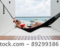 Back view of woman in red bikini resting in hammock with ocean view on rooftop of a luxury hotel. 89299386