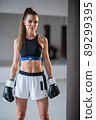 Portrait of a young attractive girl boxer in the gym wearing gloves next to a punching bag 89299395