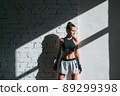 Beautiful contrasting portrait with the play of light and shadow of a young and fit girl in a loft interior with a white brick wall 89299398