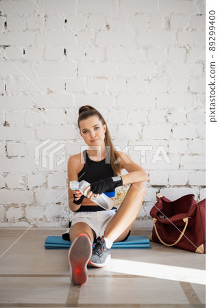 Female fighter exhausted after exercise feeling dehydration, drinks isotonic drink from bottle. Young woman rest after intense training in a boxing studio. 89299400
