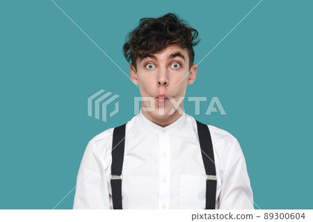 Funny surprised man with fish lips, big eyes looking at camera. Portrait of handsome hipster curly young businessman in classic casual white shirt, suspender. studio shot isolated on blue background. Funny surprised man with fish lips, big eyes looking at camera. Portrait of handsome hipster curly young businessman in classic casual white shirt, suspender. studio shot isolated on blue background. 89300604