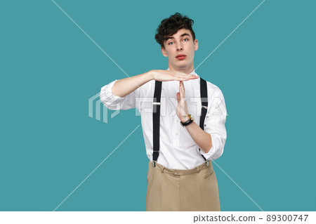 I need more time. man showing timeout gesture. Portrait of handsome hipster curly young businessman in classic casual white shirt and suspender standing. indoor studio shot isolated on blue background 89300747