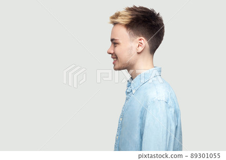 Profile side view portrait of happy handsome young man in light blue shirt standing with toothy smile and looking forward with happiness. indoor studio shot on grey background copy space. Profile side view portrait of happy handsome young man in light blue shirt standing with toothy smile and looking forward with happiness. indoor studio shot on grey background copy space. 89301055